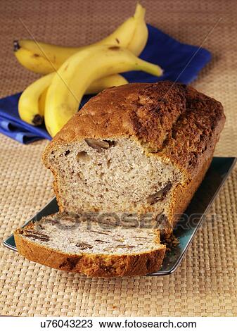 Stock Image - Whole Banana Walnut Bread Or Loaf With One Cut Slice, On Tabletop With Fresh Bananas In Background. Fotosearch