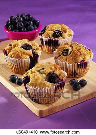 Stock Image - Wooden Board With Four Blueberry Muffins And Small Pink Bowl With Fresh Blueberries, Purple Tabletop. Fotosearch