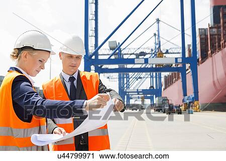 Stock Image - Engineers looking at blueprint in shipping yard. Fotosearch
