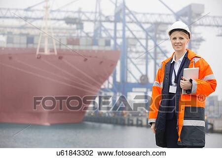 Stock Image - Female engineer holding tablet PC in shipping yard. Fotosearch