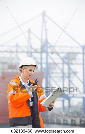 Female engineer looking at clipboard using walkie-talkie in shipping yard View Large Photo Image Stock Image - Female engineer looking at clipboard using walkie-talkie in shipping yard. Fotosearch