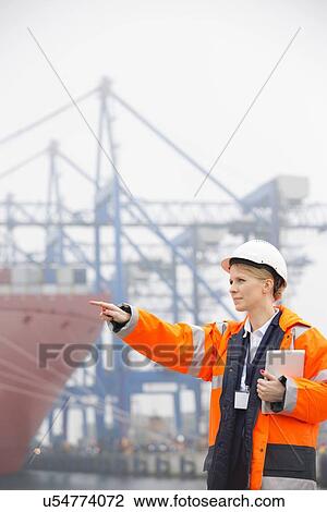 Female engineer pointing away while holding tablet PC in shipping yard View Large Photo Image Stock Image - Female engineer pointing away while holding tablet PC in shipping yard. Fotosearch