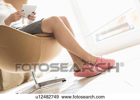 Low section of businesswoman using digital tablet on seat at home View Large Photo Image Stock Photo - Low section of businesswoman using digital tablet on seat at home. Fotosearch