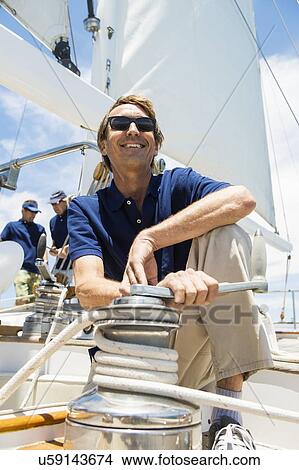 Picture - Man handling yacht winch with sailing crews in background. Fotosearch