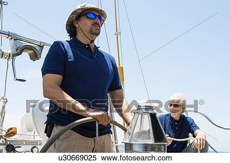 Stock Photography - Man steering sailboat with male friend sitting in background. Fotosearch
