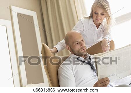 Mid adult business couple reading newspaper at home View Large Photo Image Stock Photograph - Mid adult business couple reading newspaper at home. Fotosearch