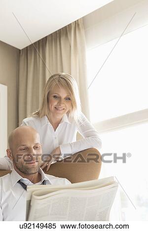 Stock Photography - Mid adult business couple reading newspaper at home. Fotosearch