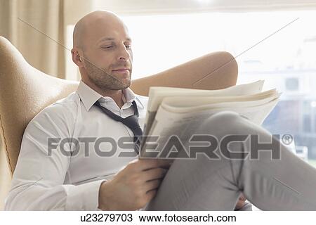 Mid adult businessman reading newspaper on chair at home View Large Photo Image Stock Image - Mid adult businessman reading newspaper on chair at home. Fotosearch