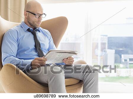 Mid adult businessman reading newspaper on wing back chair at home View Large Photo Image Stock Photo - Mid adult businessman reading newspaper on wing back chair at home. Fotosearch