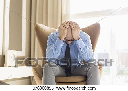 Stock Photography - Mid adult businessman with hands on head sitting on chair at home. Fotosearch
