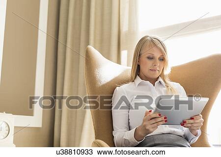 Mid adult businesswoman using digital tablet on wing back chair at home View Large Photo Image Stock Image - Mid adult businesswoman using digital tablet on wing back chair at home. Fotosearch