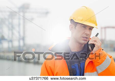 Mid adult man using walkie-talkie in shipping yard View Large Photo Image Stock Photograph - Mid adult man using walkie-talkie in shipping yard. Fotosearch