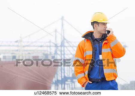 Mid adult man using walkie-talkie in shipping yard View Large Photo Image Stock Photography - Mid adult man using walkie-talkie in shipping yard. Fotosearch