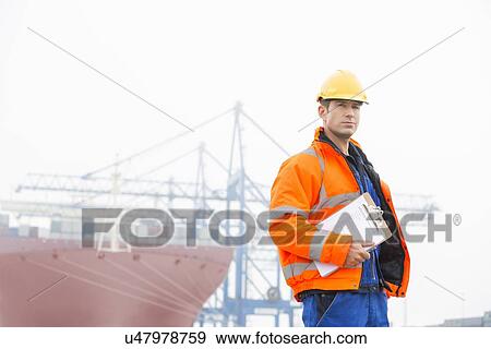 Stock Photo - Mid adult man with clipboard in shipping yard. Fotosearch