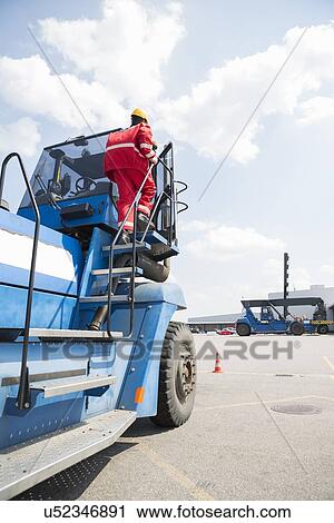 Mid adult worker getting on forklift truck in shipping yard View Large Photo Image Stock Image - Mid adult worker getting on forklift truck in shipping yard. Fotosearch