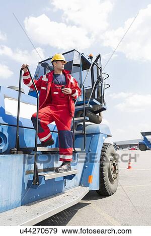 Mid adult worker standing on forklift truck in shipping yard View Large Photo Image Stock Photo - Mid adult worker standing on forklift truck in shipping yard. Fotosearch