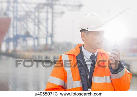 Stock Image - Middle-aged man using walkie-talkie in shipping yard. Fotosearch