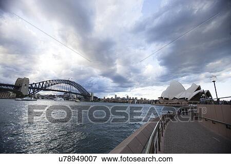 Stock Photo - View of Opera House and Harbor Bridge against cloudy sky, Sydney, Australia. Fotosearch