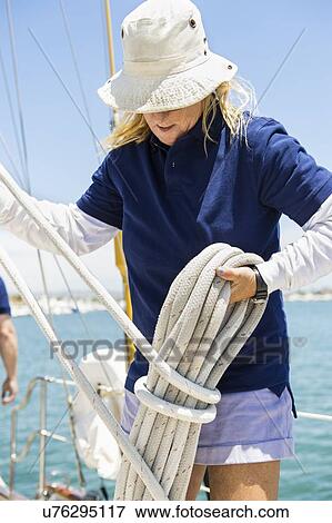 Stock Photo - Woman coiling up rope on yacht. Fotosearch