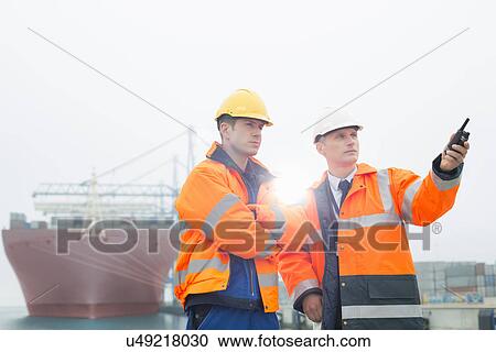 Stock Image - Workers conversing in shipping yard. Fotosearch