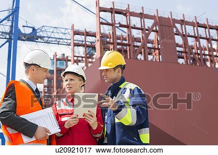 Stock Photo - Workers discussing in shipping yard. Fotosearch