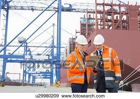 Stock Photo - Workers discussing over clipboard in shipping yard. Fotosearch
