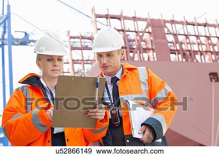 Workers discussing over clipboard in shipping yard View Large Photo Image Stock Photo - Workers discussing over clipboard in shipping yard. Fotosearch