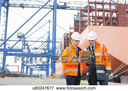 Stock Photo - Workers discussing over clipboard in shipping yard. Fotosearch