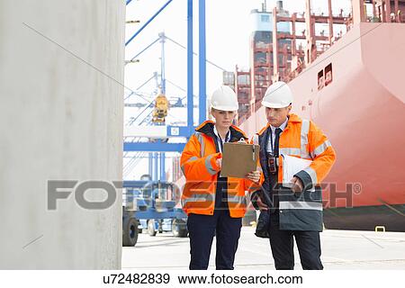 Workers discussing over clipboard in shipping yard View Large Photo Image Stock Photo - Workers discussing over clipboard in shipping yard. Fotosearch
