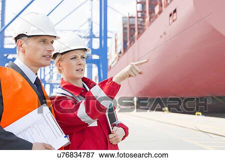 Workers discussing over clipboard in shipping yard View Large Photo Image Stock Photo - Workers discussing over clipboard in shipping yard. Fotosearch