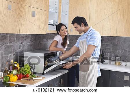 Stock Image - Beautiful woman looking at man preparing food in kitchen. Fotosearch