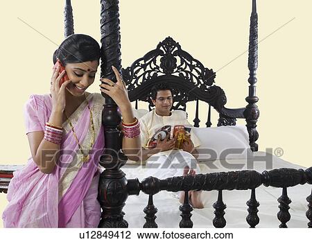 Stock Image - Bengali woman stitching while husband reads a magazine . Fotosearch