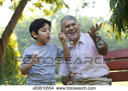 Picture - Boy blowing bubbles in a park while grandfather looks on. Fotosearch
