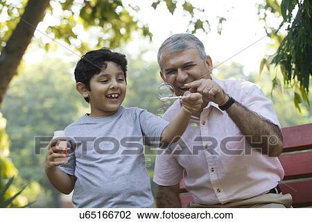 Boy blowing bubbles in a park while grandfather looks on View Large Photo Image Stock Image - Boy blowing bubbles in a park while grandfather looks on. Fotosearch