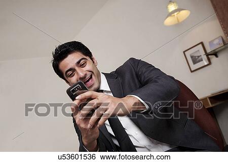 Businessman laughing at an sms on his phone View Large Photo Image Stock Photograph - Businessman laughing at an sms on his phone . Fotosearch