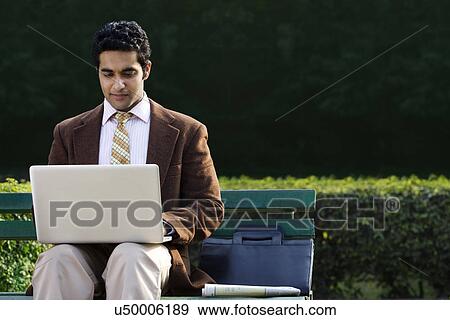 Businessman working on a laptop in a park View Large Photo Image Stock Photo - Businessman working on a laptop in a park . Fotosearch