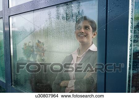 Businesswoman looking out of a window View Large Photo Image Picture - Businesswoman looking out of a window . Fotosearch