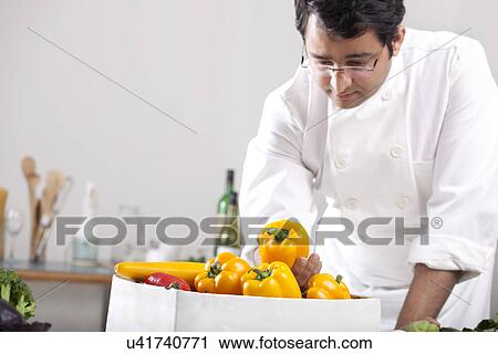 Stock Image - Chef inspecting yellow bell peppers . Fotosearch