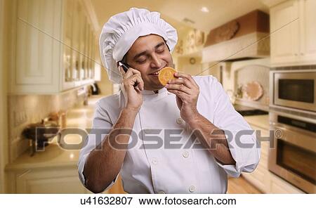 Chef talking on a mobile phone and smelling a cookie View Large Photo Image Stock Photo - Chef talking on a mobile phone and smelling a cookie . Fotosearch