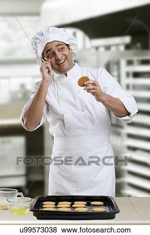 Stock Photo - Chef talking on a mobile phone holding a cookie . Fotosearch
