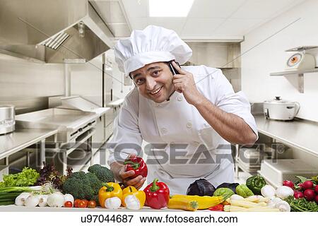 Chef talking on a mobile phone while holding a bell pepper View Large Photo Image Stock Photo - Chef talking on a mobile phone while holding a bell pepper . Fotosearch