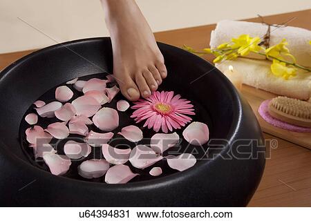 Stock Image - Close-up of a woman's feet and a bowl filled with water and rose petals . Fotosearch