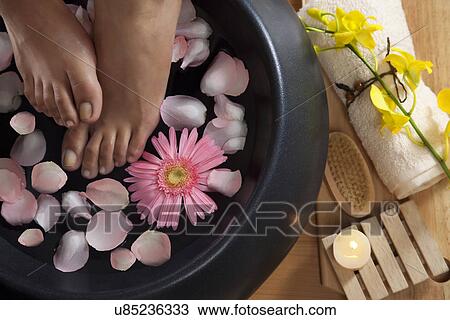 Stock Image - Close-up of woman's feet in a bowl of water and petals at spa . Fotosearch