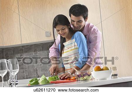 Stock Image - Couple cutting vegetables together in kitchen. Fotosearch