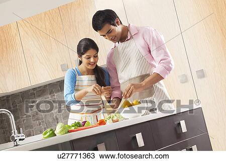 Stock Image - Couple preparing fresh vegetable salad in kitchen. Fotosearch