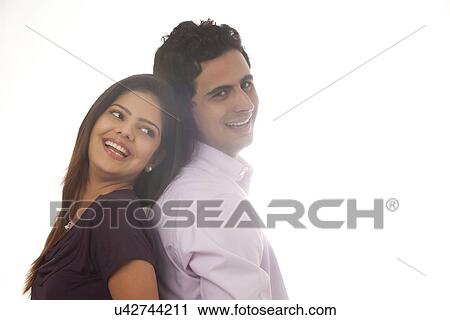 Stock Image - Couple standing back to back smiling. Fotosearch