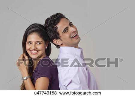 Stock Photo - Couple standing back to back smiling. Fotosearch