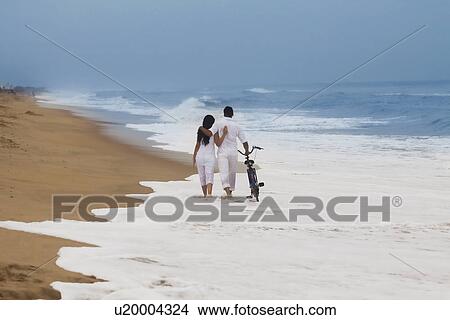 Couple walking on a beach with a bicycle View Large Photo Image Picture - Couple walking on a beach with a bicycle . Fotosearch