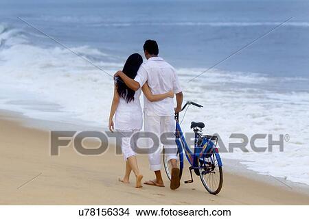 Picture - Couple walking on a beach with a bicycle . Fotosearch