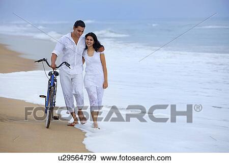 Couple walking on a beach with a bicycle View Large Photo Image Stock Photo - Couple walking on a beach with a bicycle . Fotosearch